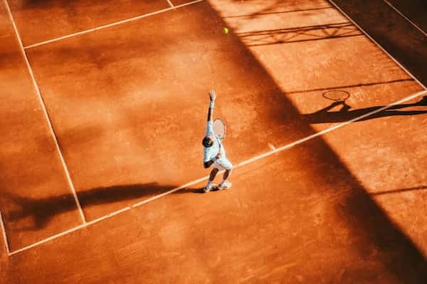 Joueur de tennis au service sur une terre battue, vu du dessus